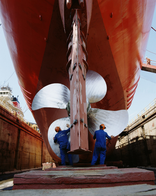 Two men working on propeller of ship on dry dock